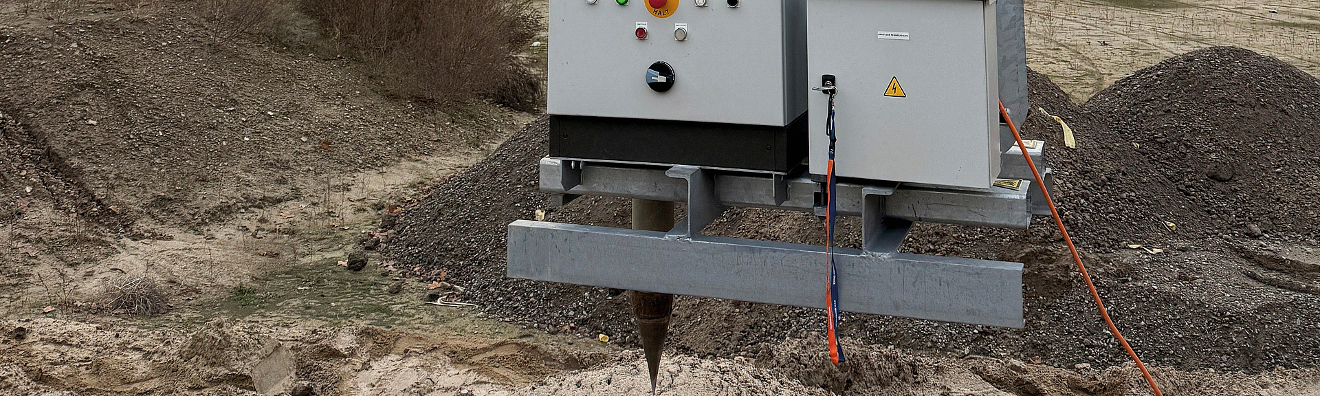 Bohrlochstopfmaschine wird mit einem Bagger auf einer Baustelle in den Boden eingesetzt, im Hintergrund steht ein Kuppelbau.
