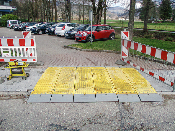 Ein Baugraben, der quer unterhalb einer Straße verläuft, ist mit Kunststoff-Überfahrplatten abgedeckt. Diese sind durch ihre gelbe Signalfarbe sehr gut sichtbar.