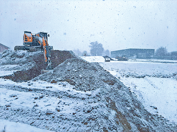 Aushubarbeiten vor dem Neubau des Polizeigebäudes  Baustelle mit Schnee. Auf dem Aushubhügel befindet sich ein Bagger.