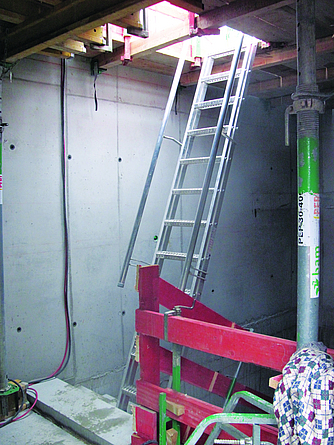 Stufenleiter mit seitlichenHandläufen, die aus einem Treppenhaus im Bauzustand über eine geöffnete Luke ins Freie führt