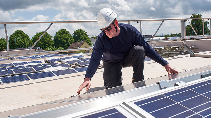 Arbeit an Photovoltaikanlage Ein Bauarbeiter mit Schutzhelm arbeitet an einer Photovoltaikanlage auf einem Dach.