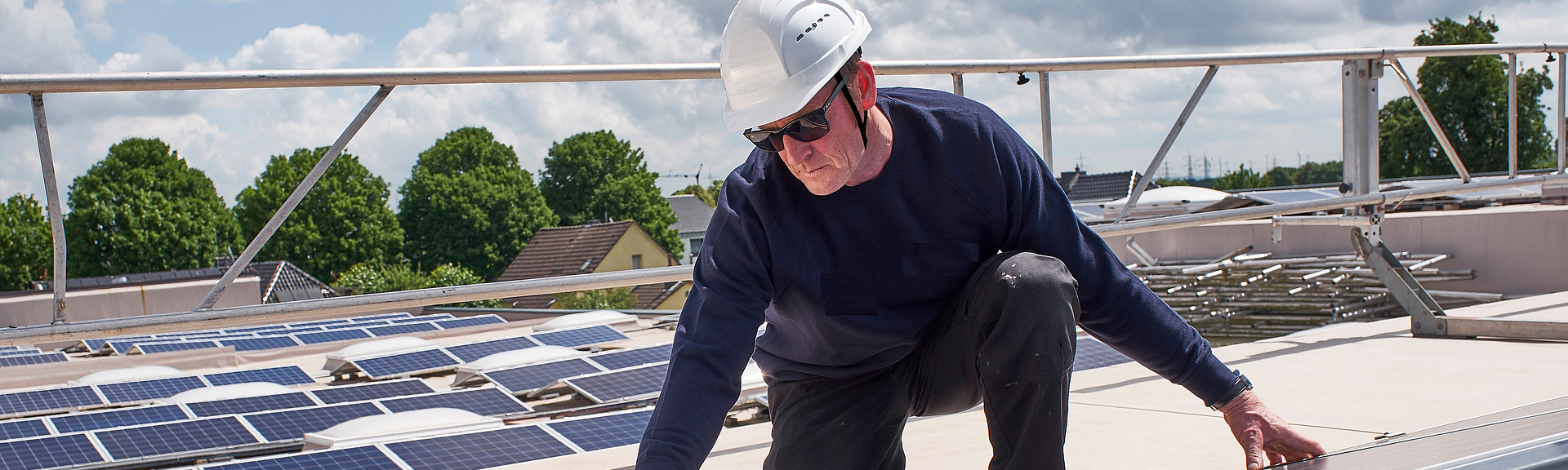 Ein Bauarbeiter mit Schutzhelm arbeitet an einer Photovoltaikanlage auf einem Dach.