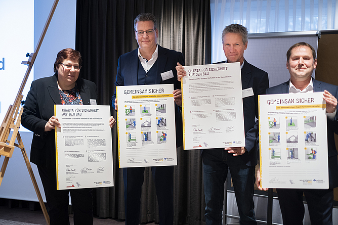 Vier Personen vom Abbruchverband Nord und der BG BAU halten die unterzeichnete „Charta für Sicherheit auf dem Bau“ in Großformat.