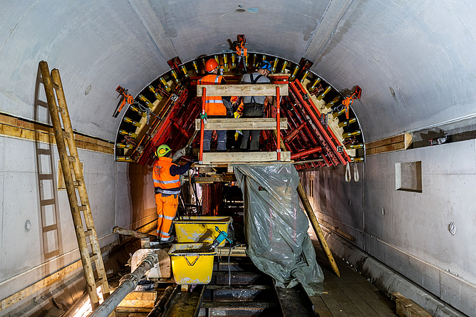 Drei Personen mit Schutzkleidung und Helm arbeiten an der Tunneldecke.