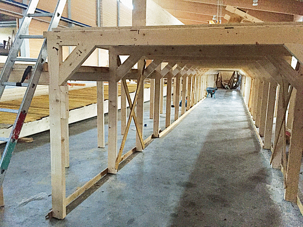 Langes Holzgestell in einer Halle an an dessen Seite eine Leiter steht.