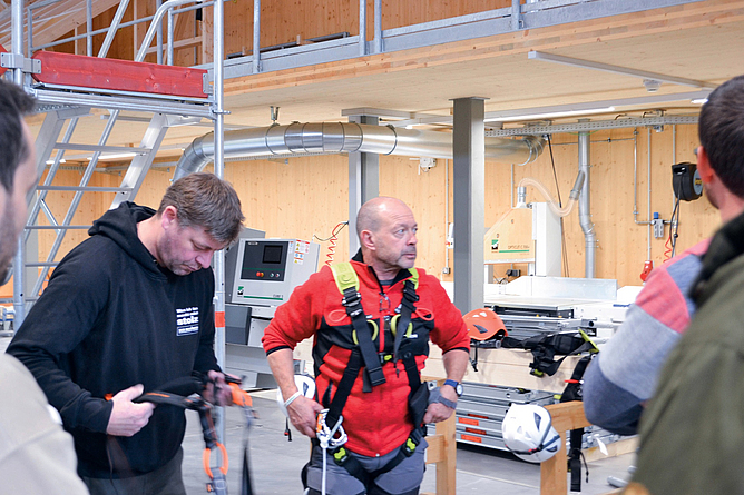 Der Landesinnungsverband des Bayerischen Zimmererhandwerks bietet seinen Mitgliedern eine intensive Weiterbildungsveranstaltung Zwei Männer üben das Anlegen der PSA gegen Absturz in der Trainingshalle des BZ Immenstadt.