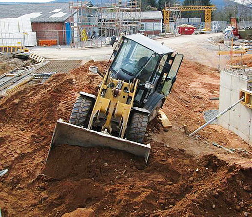 Halb umgekippter Radlader im Böschungsbereich einer Baustelle. Der Maschinenführer will gerade herausspringen.