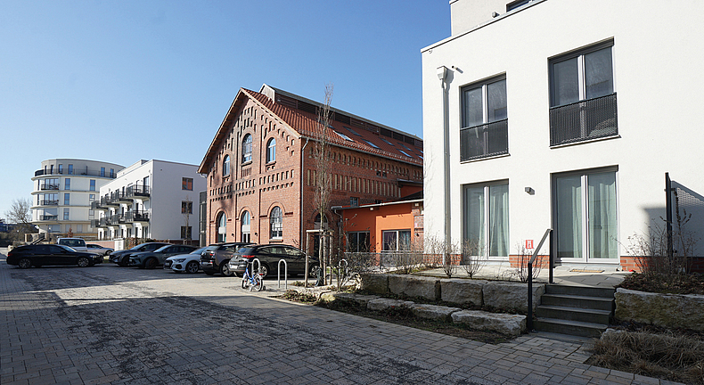 Backsteingebäude neben modernen Wohnhäusern mit parkenden Autos im Vordergrund.