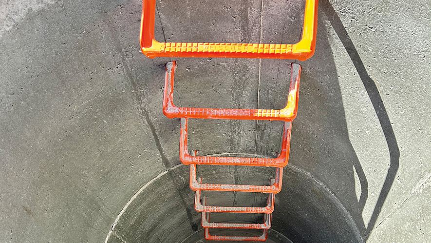 Abwasserschacht mit fest verbauten Steigeisen Blick von oben in einen runden Betonschacht mit fest installierten orangenen Steigeisen.