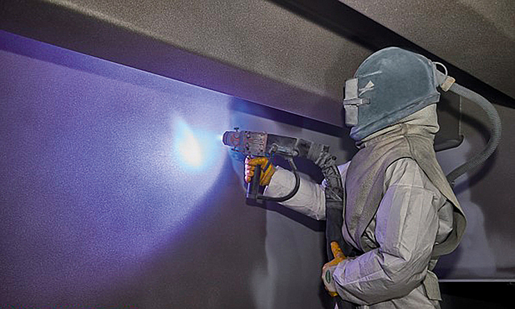 Das Lichtbogen-Spritzverfahren stellt hohe Ansprüche an den Arbeitsschutz für die ausführenden Beschäftigten. Ein Stahlbauteil wird per von einem Beschäftigten mit persönlicher Schutzausrüstung im Metallspritzverfahren verzinkt.