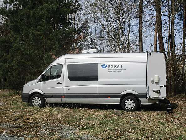 Weißes Messfahrzeug mit BG BAU-Logo steht auf einer Freifläche am Waldrand.