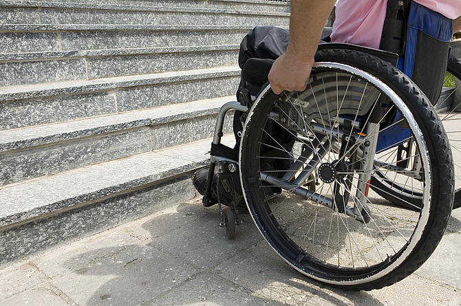 Ein Mann sitzt im Rollstuhl vor einer Treppe.