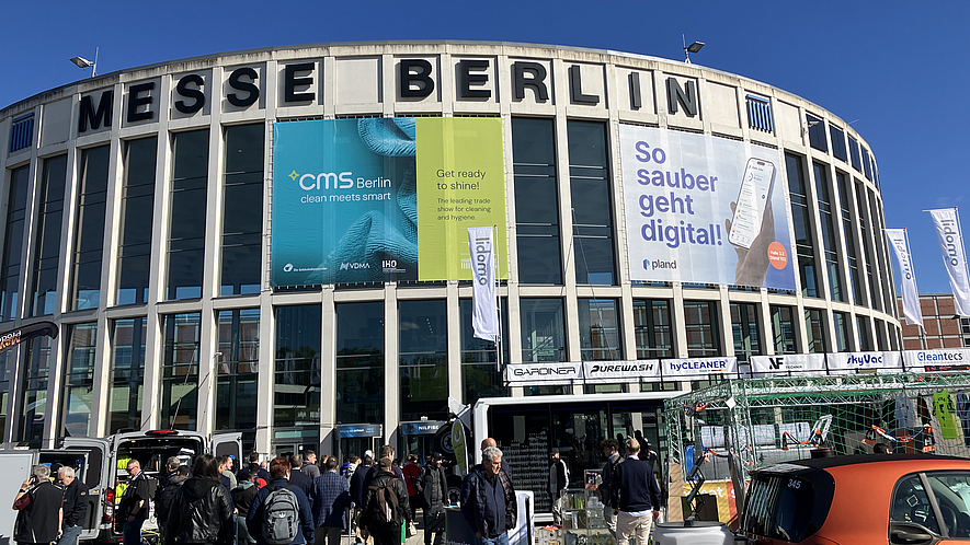 Eingangsgebäude Süd der Messe Berlin, das mit CMS Fahnen behangen ist. Vor dem Gebäude besuchen Gäste die Outdoor-Messestände. 