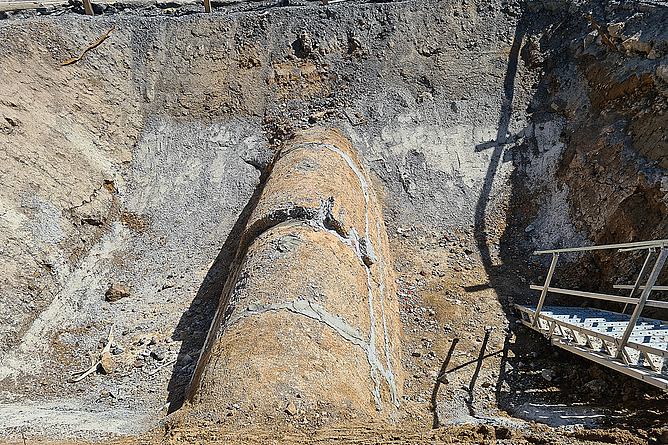 Nach Abschluss der Ringraumverfüllung wird die zwischengelagerte Haube des Altkanals wieder eingebaut. Mulde mit einem schmalen Kanal. Dieser Kanal wurde mit einer Haube verschlossen, sodass nur noch eine schmale Öffnung zu sehen ist.