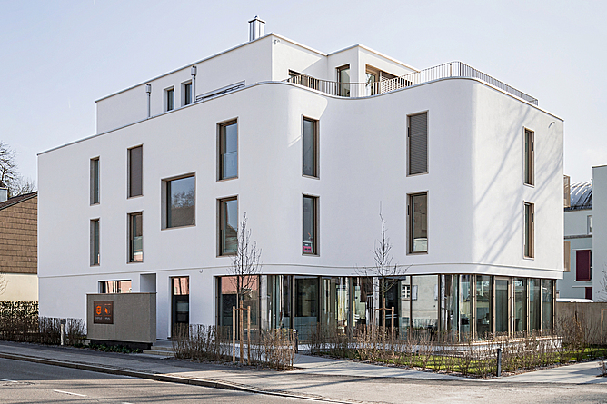 Blick auf ein weißes Gebäude mit einer geschwungenen Außenwand von der anderen Straßenseite aus.