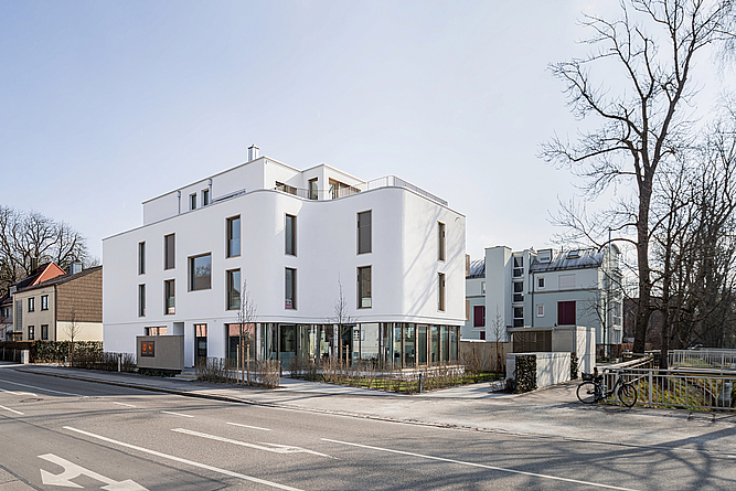 Blick auf ein weißes Gebäude mit einer geschwungenen Außenwand von der anderen Straßenseite aus.