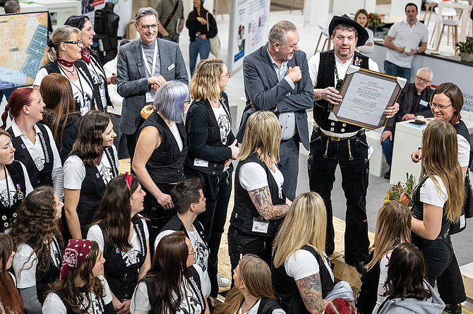 Gruppe von Dachdeckern steht in einer Messehalle zusammen, eine Person hält eine gerahmte Auszeichnung.