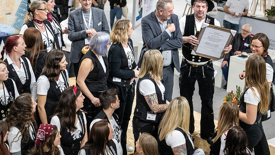 Gruppe von Dachdeckern steht in einer Messehalle zusammen, eine Person hält eine gerahmte Auszeichnung.