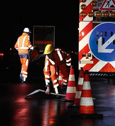 Warnkleidung beim Arbeiten in Dunkelheit Zwei Bauarbeiter arbeiten in der Dunkelheit auf einer Straße. Sie tragen sichtbare Warnkleidung.