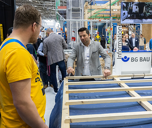 Ein Mann zeigt Messebesuchern auf der BAU den Montagetisch.