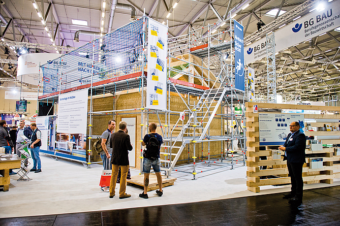 Messestand mit offenem Holzhaus, an dem draußen Gerüste und Treppen angebracht sind.