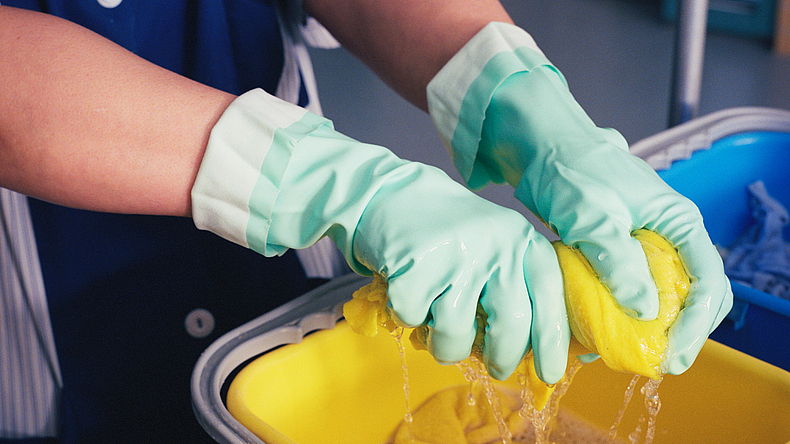 Abwaschen mit Handschuhen und Lappen über einem wassergefüllten Eimer.