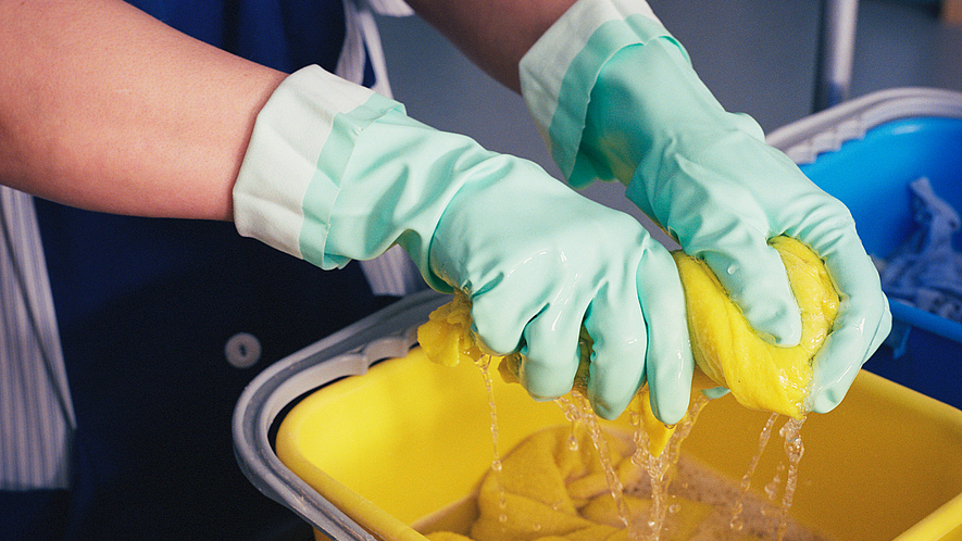 Abwaschen mit Handschuhen und Lappen über einem wassergefüllten Eimer.