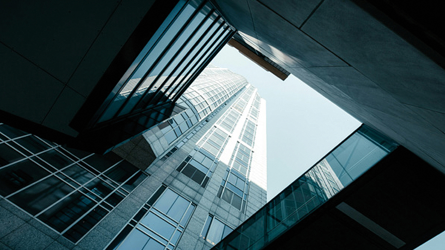 Titelblatt des TÜV-Baurechtsreports 2025: Die untere Hälfte enthält ein Bild, das einen Blick von unten auf ein modernes Hochhaus mit Glas- und Stahlfassade zeigt.