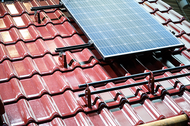 Dachfläche mit braunen Ziegeln, auf der Solarpaneele angebracht sind.