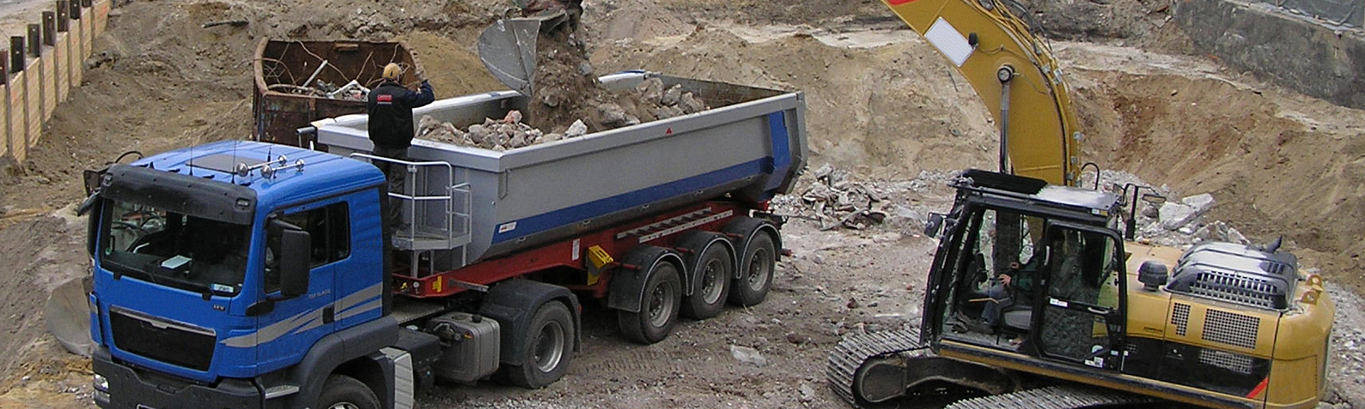 Ein LKW wird auf einer Baustelle von einem Bagger beladen.