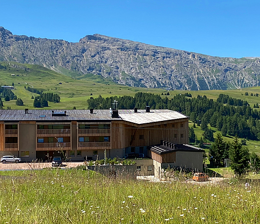 Seitenansicht des Holzgebäudes inmitten einer Wiese in den Alpen.