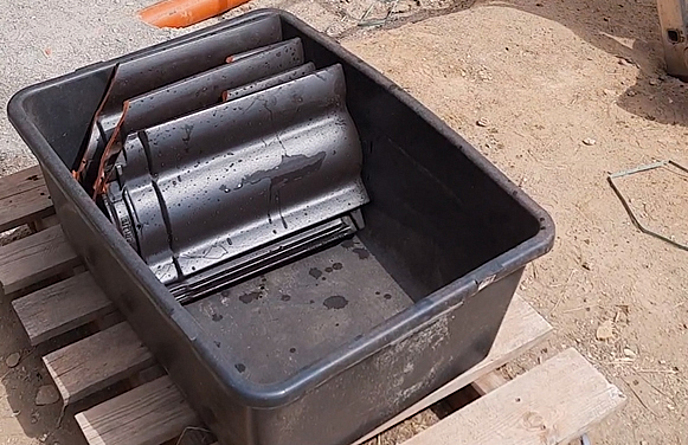 Dunkle, leicht benässte Ziegel in einer Kiste hintereinander gestapelt.