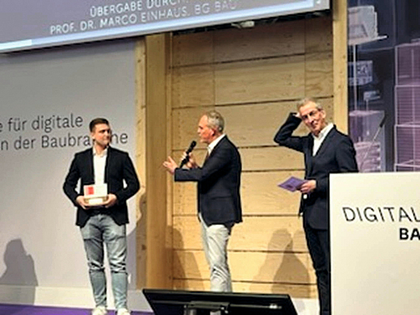 Verleihung des Deutschen Baupreises 2024 durch Marco Einhaus, BG BAU, an Heitkamp & Hülscher Marco Einhaus mit Mikro in der Hand spricht zu einem Mann, der einen Preis in der Hand hält.