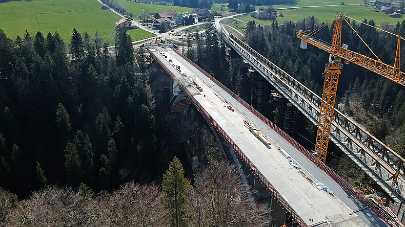 Die neue Konstruktion samt neuer Bögen über den alten Melan-Bögen der Echelsbacher Brücke dient dem Schutz des zu bewahrenden Denkmals. Blick von oben auf die Brückenbaustelle mit Kran.