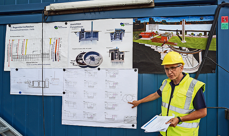 Bauleiter vor Bauplänen und Zeichnungen erklärt den Bau desÜberlaufbeckens.