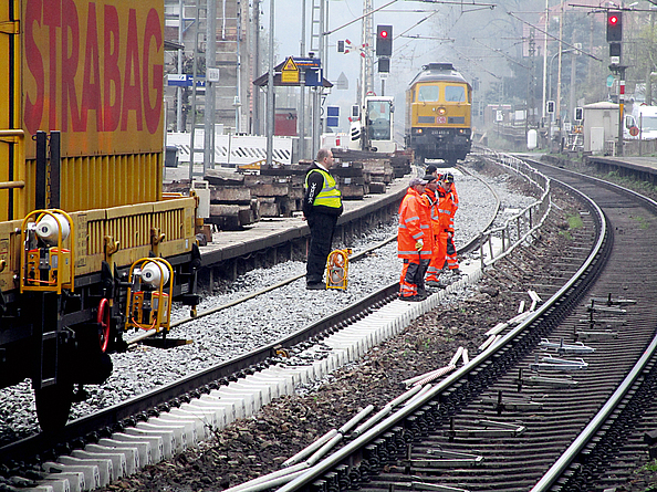 Eine Gruppe mit mehreren Beschäftigten in signalfarbener Warnkleidung nimmt Arbeiten an einem Bahngleis vor.