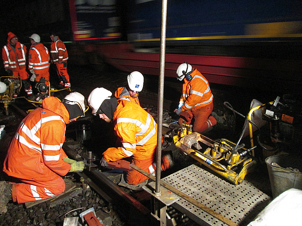 Mehrere Personen in Warnkleidung führen nachts Arbeiten an einem Bahngleis mit Spezialwerkzeug und Maschinen durch.