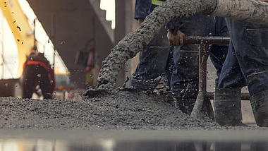 Auf einer Rohbau-Baustelle wird Beton aus einem Rohr auf den Boden gelassen. 