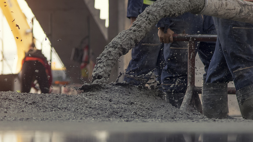 Auf einer Rohbau-Baustelle wird Beton aus einem Rohr auf den Boden gelassen. 
