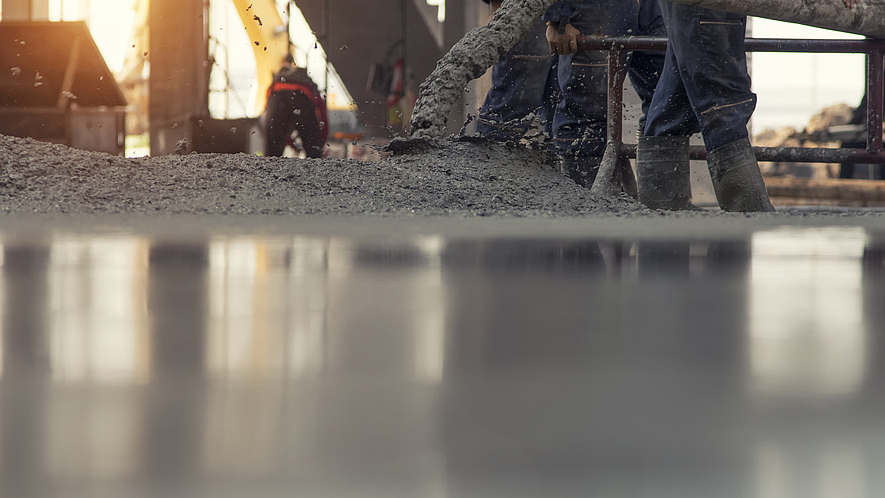 Auf einer Rohbau-Baustelle wird Beton aus einem Rohr auf den Boden gelassen. 