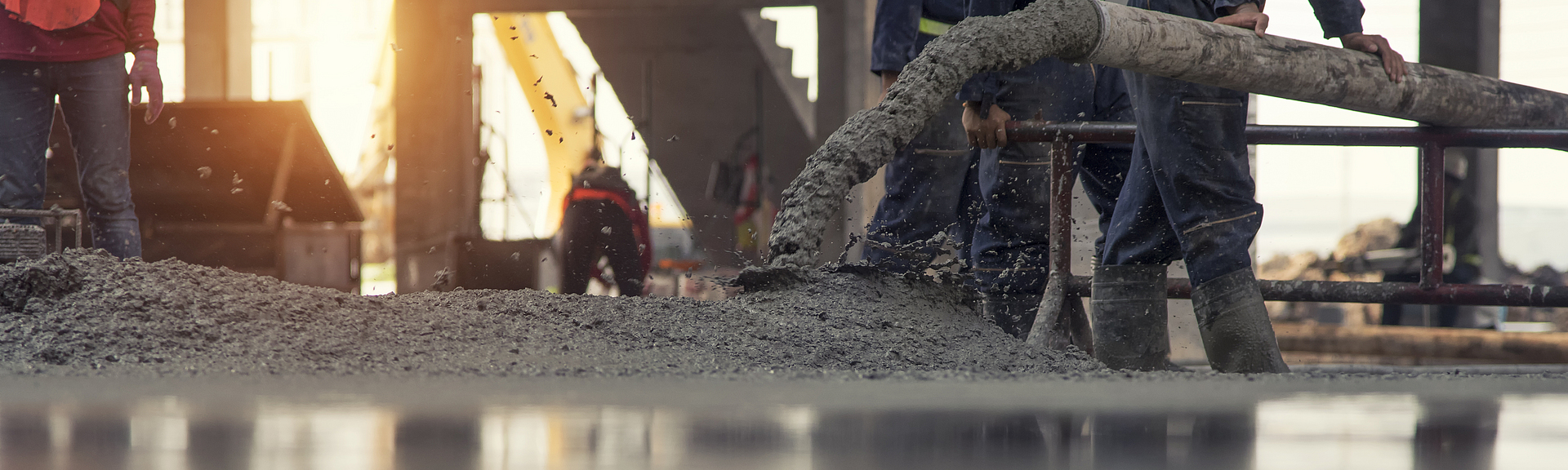 Auf einer Rohbau-Baustelle wird Beton aus einem Rohr auf den Boden gelassen. 