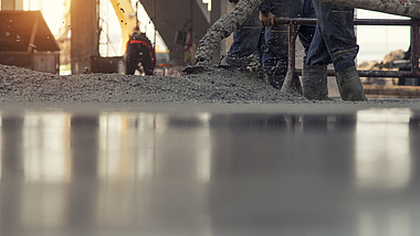 Auf einer Rohbau-Baustelle wird Beton aus einem Rohr auf den Boden gelassen. 