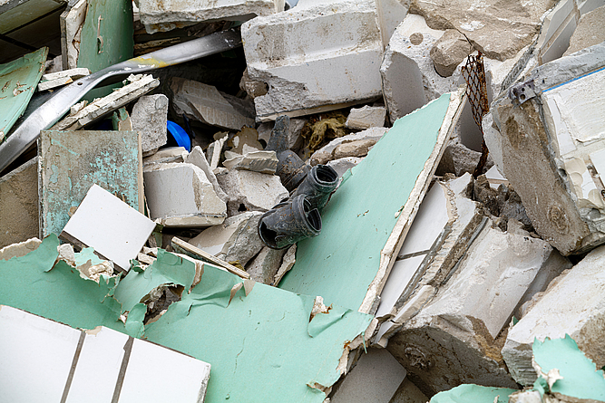 Bauabfälle aus unterschiedlichen Materialien in unsortierter Anhäufung: Mauersteine, Rigips-Platten, PVC-Rohrstücke, Aluminiumbleche.
