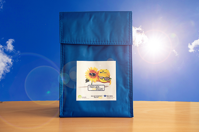 Die blaue Kühltasche des UV-Schutz-Paketes steht auf einem Tisch. Im Hintergrund ist blauer Himmel mit vereinzelten Wolken.