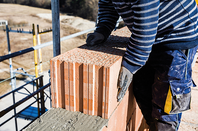 Dämmstoff-gefüllte Coriso-Mauerziegel werden von einem Beschäftigten zu einer Außenmauer aufgeschichtet