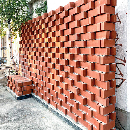 Eine etwa vier Meter lange Wand aus Ziegelsteinen, die versetzt angeordnet sind, steht auf einem Fundament.