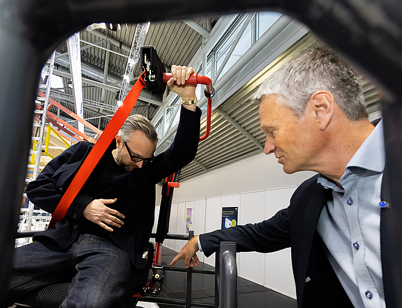 Ein Mann zeigt einem Messebesucher die Anschnallhilfe auf einem Baufahrzeug.