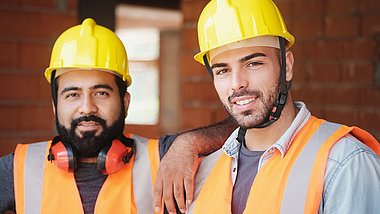 Portrait zweier Bauarbeiter auf einer Baustelle.