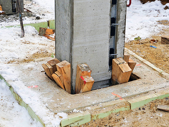 Öffnung im Fundament, in der eine Betonstütze eingehoben ist. Die Stütze wird von allen Seiten mit Holzkeilen abgestützt. 