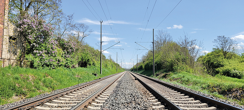 Zwei nebeneinander liegende Gleise an einer Eisenbahnstrecke mit Oberleitungen.